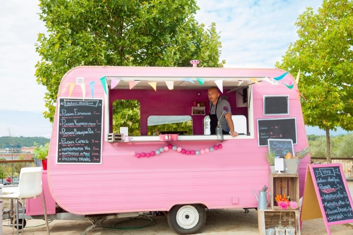 A pink vintage caravan converted into a food and drinks trailer, bunting strung along the awning and chalkboard menus mounted either side of the open hatch