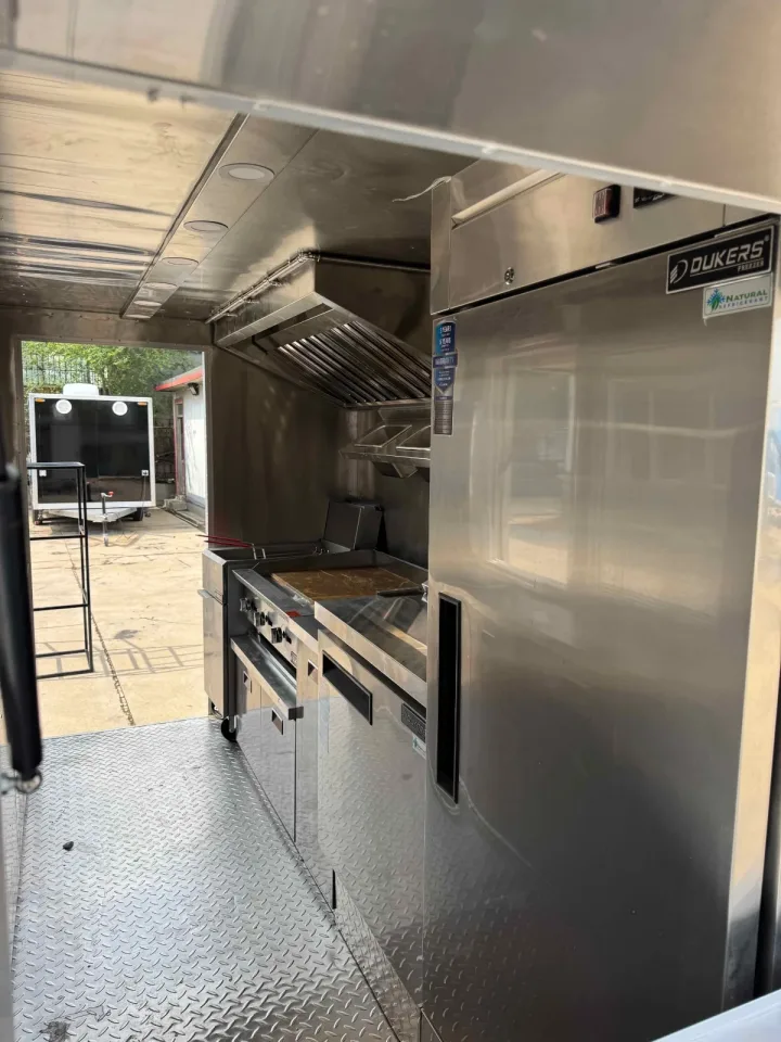 Inside a food trailer with equipment: exhaust hood, fryer and range, and a reach-in refrigerator