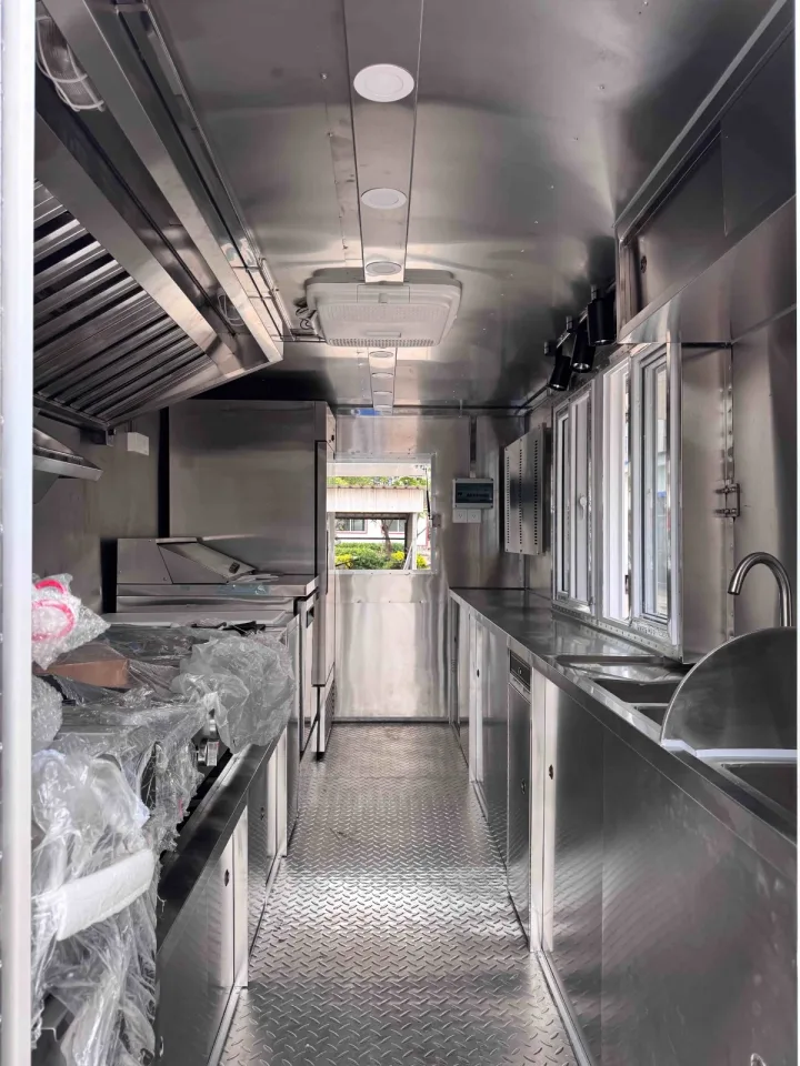 Inside a pizza food trailer: exhaust hood, stainless prep line and sinks along a diamond-plate aisle